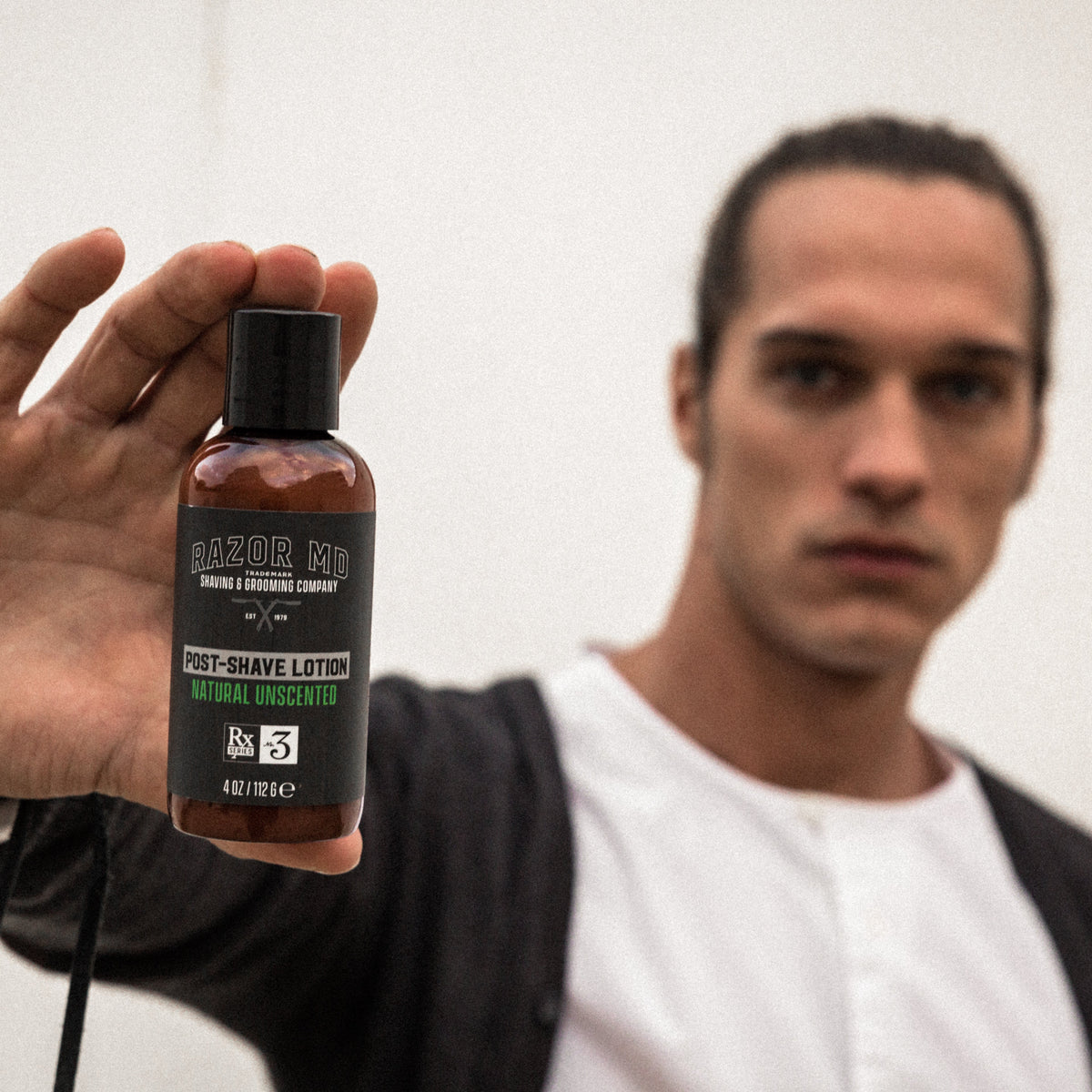 Man holding a bottle of RAZOR MD post-shave lotion with a blurred background