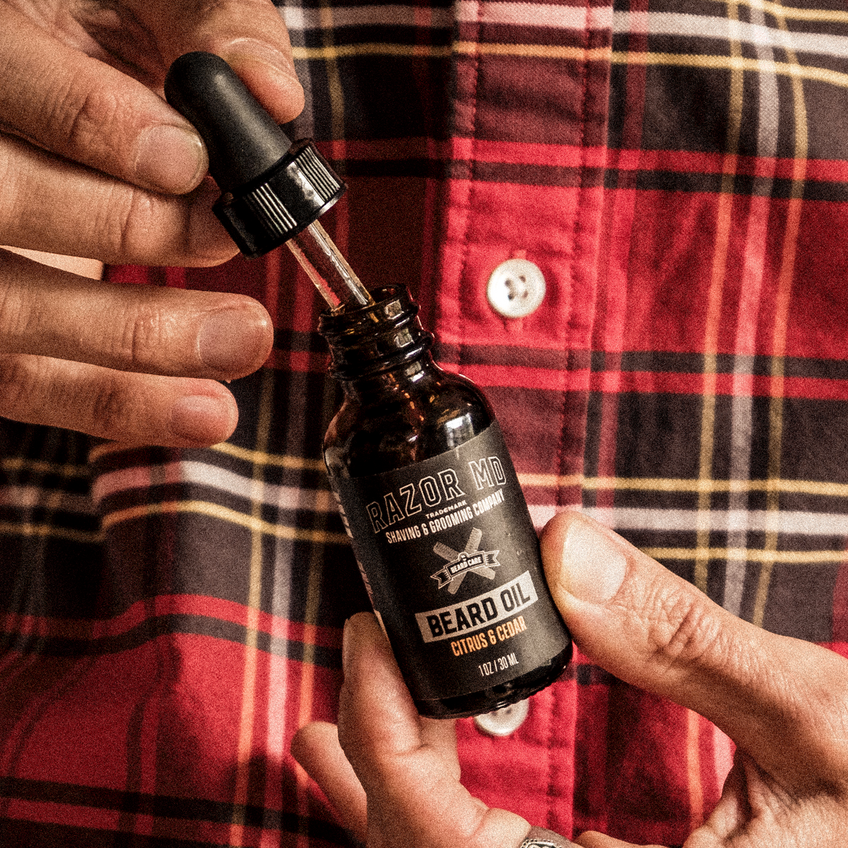 Person holding a bottle of RAZOR MD beard oil against a red plaid shirt background
