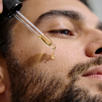 Close-up of a man applying a dropper of RAZOR MD Beard Oil to his face.